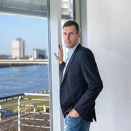 Man in blazer by window overlooking waterfront
